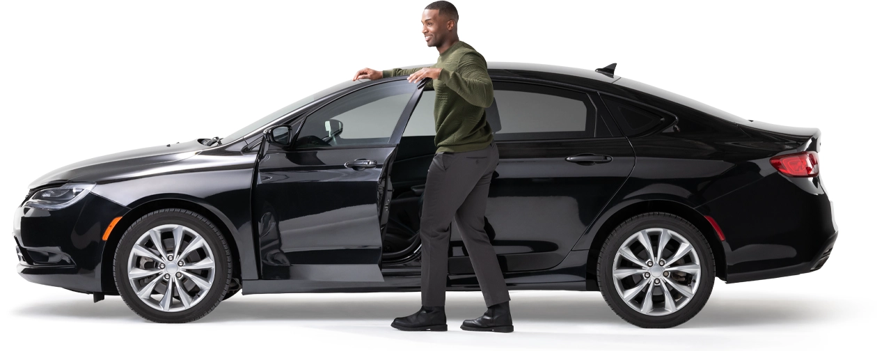 A young man stands by the open door of his midnight black car.